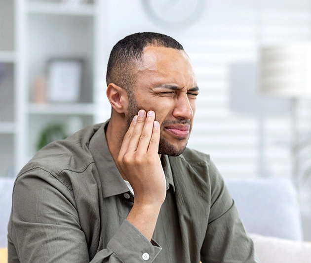 Man experiencing tooth pain, holding jaw, in modern dental office setting