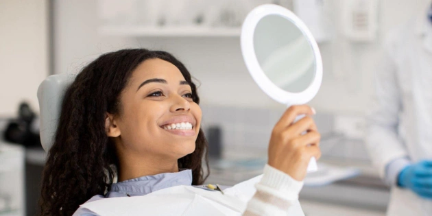 Woman holding mirror in dental office examining teeth, smiling at Carpenter Dental Group.