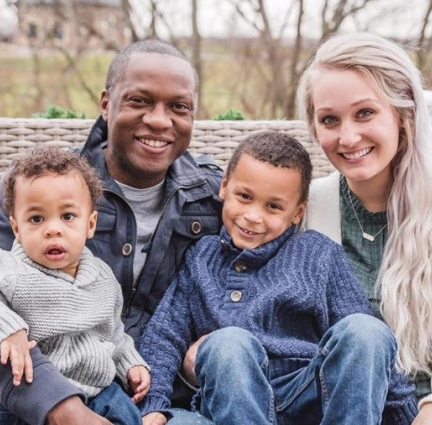 Happy multiracial family of four smiling outdoors against stone wall during fall season.